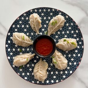 Delicious handmade momos served with spicy dipping sauce on a patterned plate.