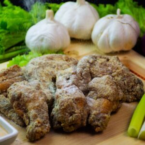 Close-up of seasoned chicken wings with fresh garlic, onions, and greens on a wooden board.