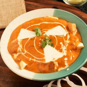 Creamy paneer makhani served in a bowl with onion rings and garnished with fresh herbs.