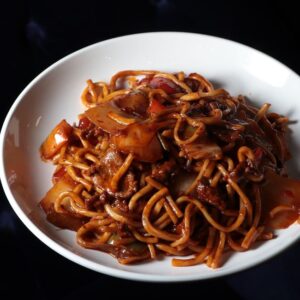 Close-up of flavorful stir-fried noodles with beef, vegetables, and savory sauce on a white plate.