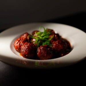 Close-up of flavorful Indo-Chinese vegetarian Manchurian served on a white plate, garnished with fresh herbs.