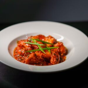 Spicy Indian paneer tikka served in a rich tomato-based gravy, garnished with green scallions.