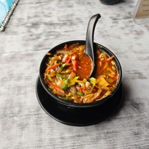 A vibrant bowl of vegetable soup served in a black dish on a textured table.