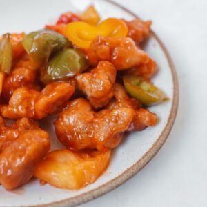 Close-up of sweet and sour chicken with bell peppers on a plate.