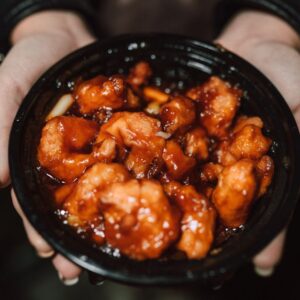 Close-up of a person holding a bowl of delicious Asian chicken dish in orange sauce.