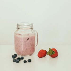 Fresh strawberry and blueberry smoothie in a glass jar with fruits on a clean surface.