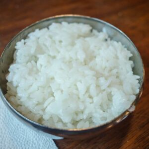 Close-up of steamed white rice in a stainless steel bowl on a wooden table.